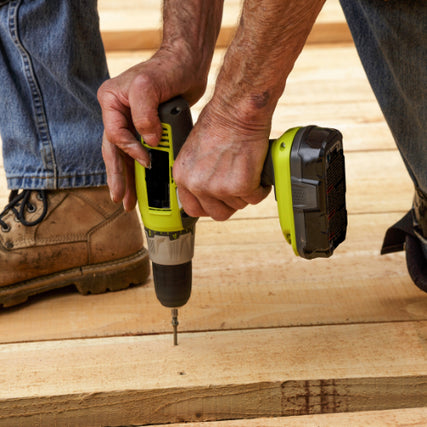 Do-It-YourselfA person in jeans and work boots uses a green cordless drill to drive a screw into wooden planks, conveying a sense of focus and craftsmanship.