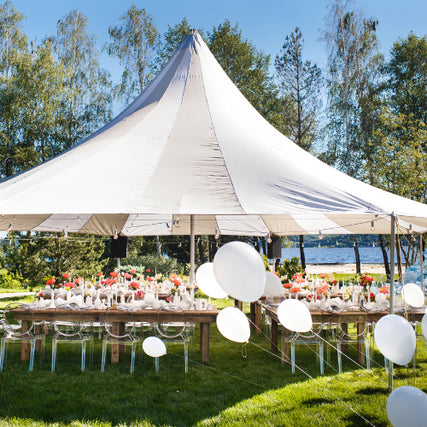 Party & EventWhite tent set up outdoors under a clear blue sky, with elegantly decorated tables and chairs surrounded by white balloons, evoking a festive atmosphere.
